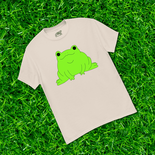 Beige t-shirt with a green frog graphic on grass