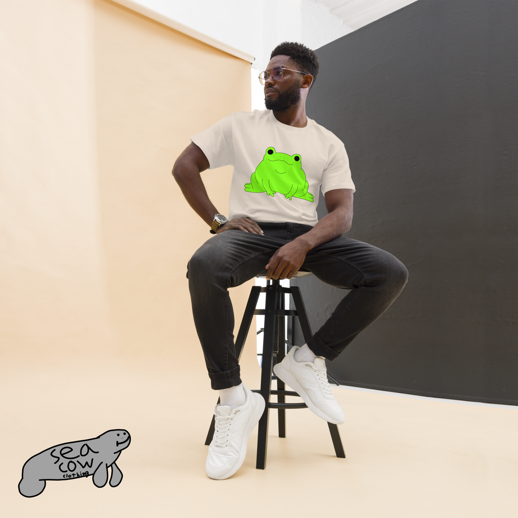 Person sitting on a stool wearing a white t-shirt with a green frog graphic, black pants, and white sneakers.