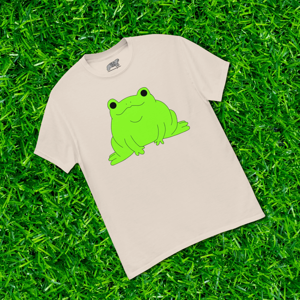 Beige t-shirt with a green frog graphic on grass
