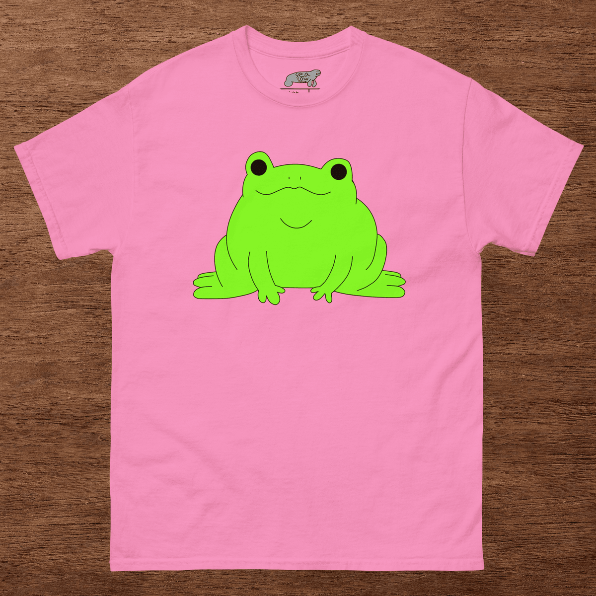 Pink t-shirt with a green frog graphic on a wooden surface