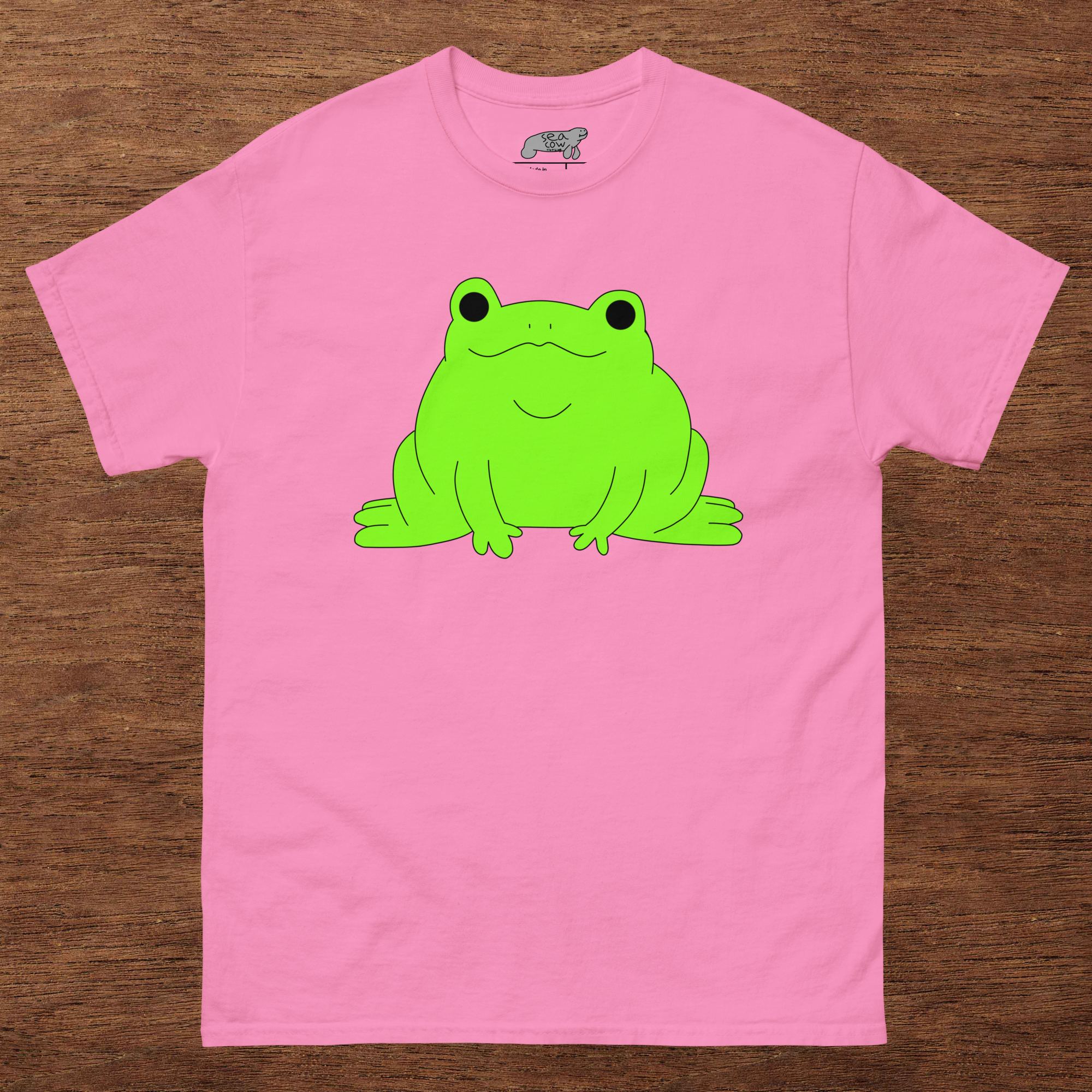 Pink t-shirt with a green frog graphic on a wooden surface