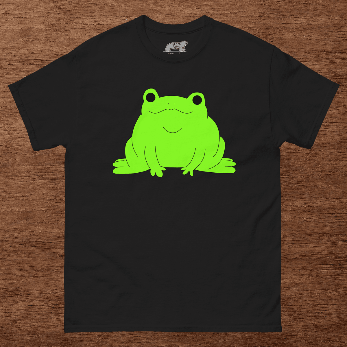 Black t-shirt with a green frog graphic on a wooden surface