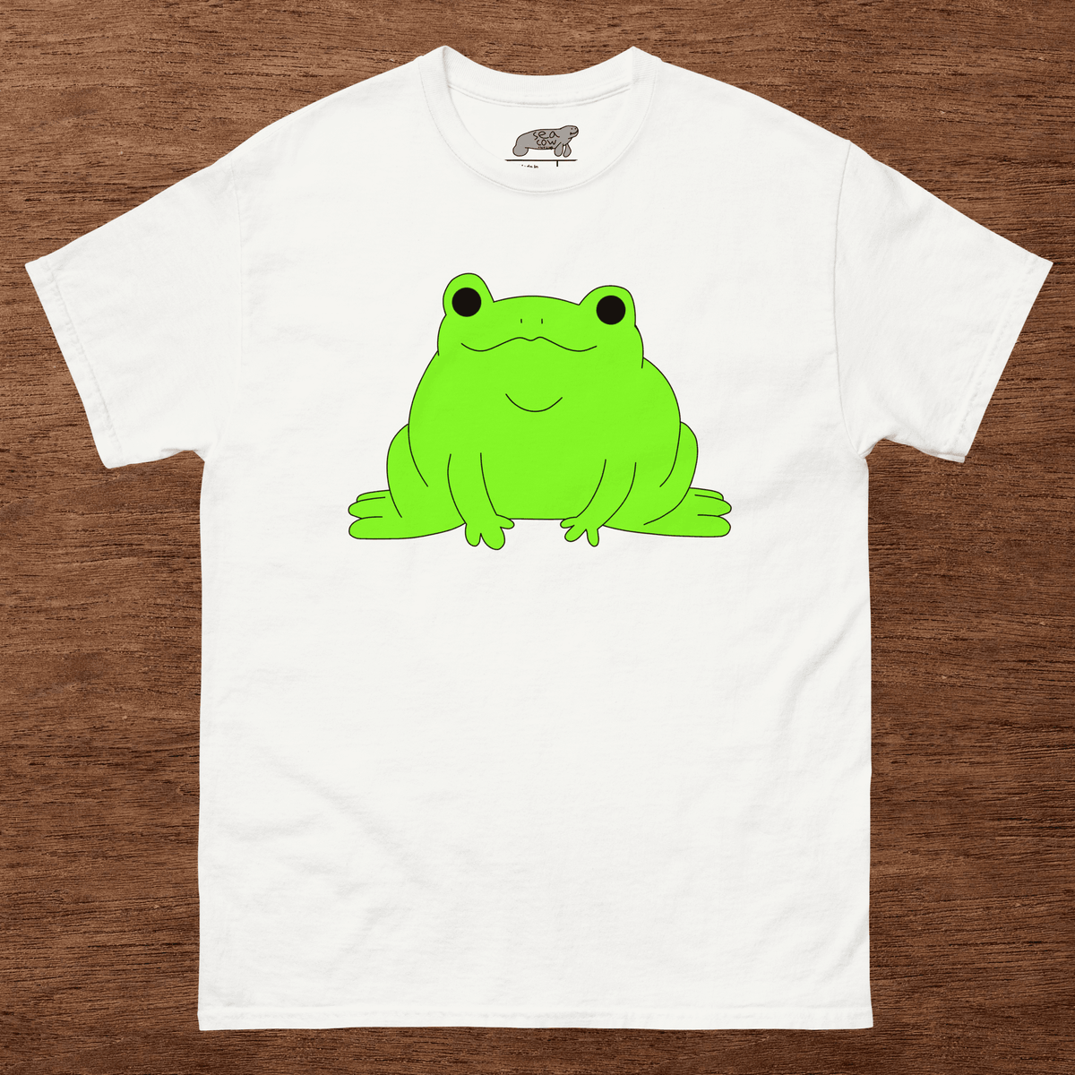 White t-shirt with a green frog graphic on a wooden surface