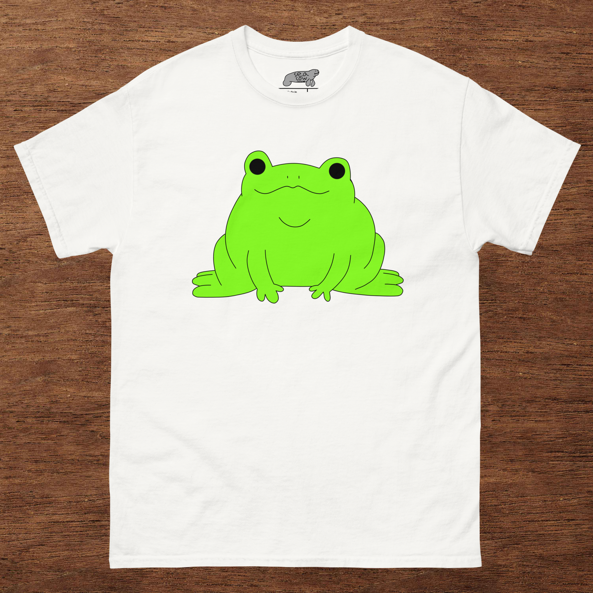 White t-shirt with a green frog graphic on a wooden surface
